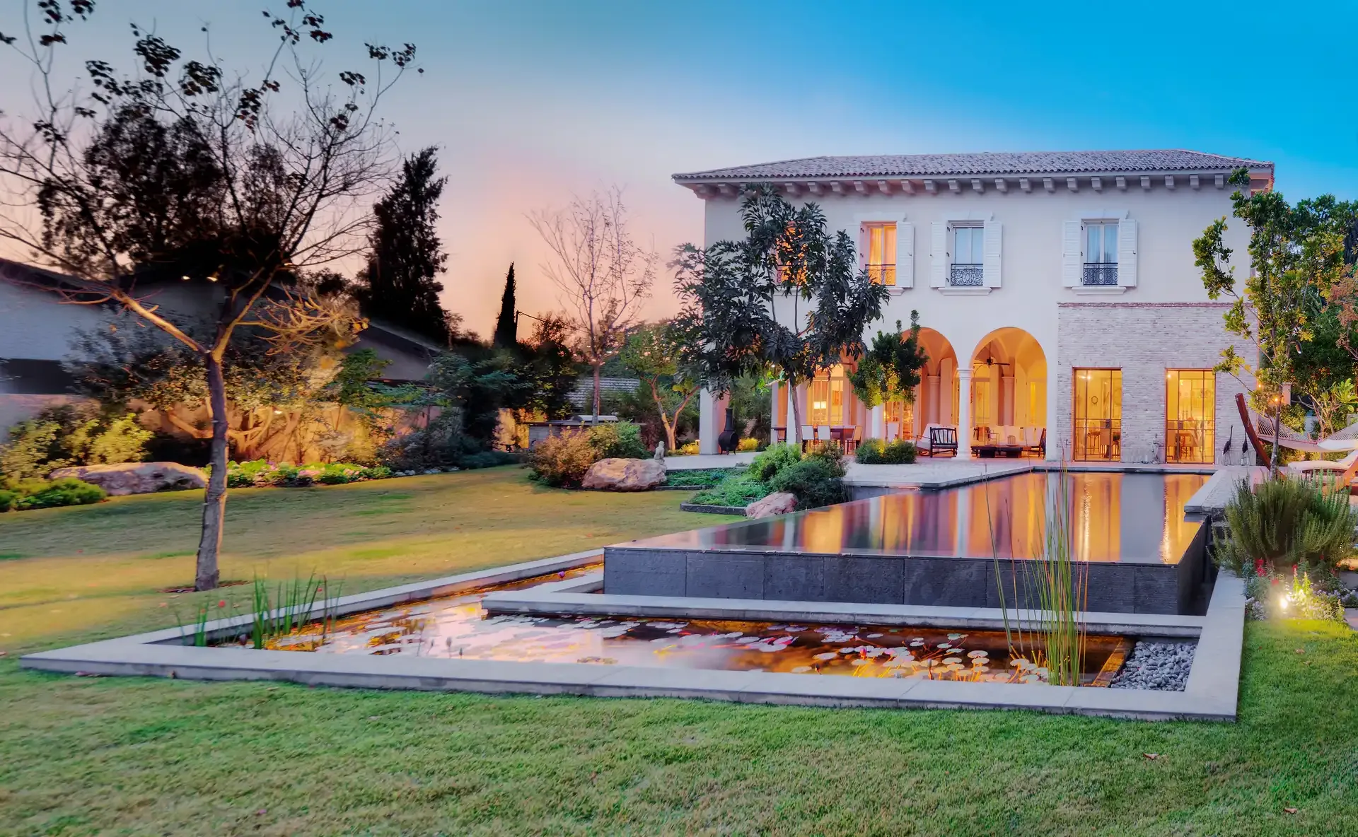 Garden with a long reflecting pool in front of a villa at dusk